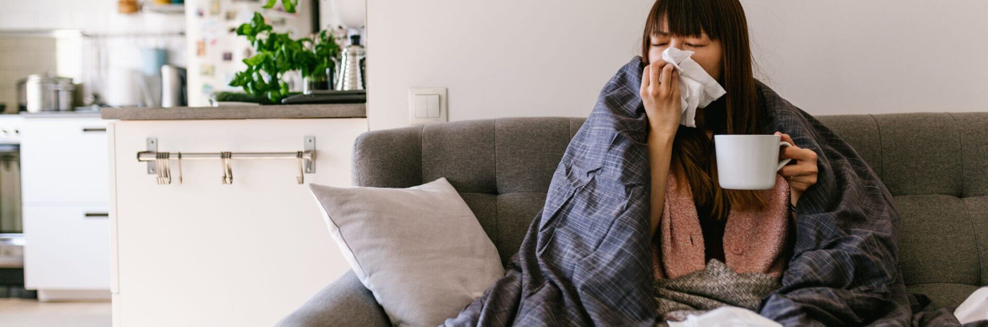 treating seasonal allergies with TCM herbal formulas - woman on couch with blanket blowing her nose and holding mug